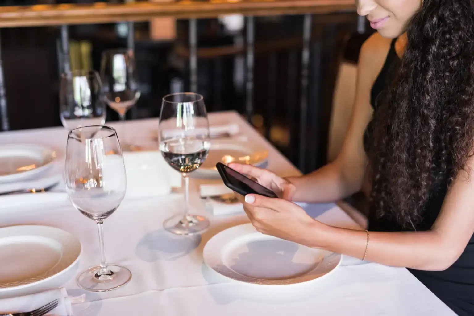 Woman at a restaurant table using her phone to make a booking