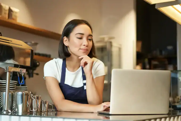 Café owner at the counter thinking while using a laptop – using AI to write your posts, the new EU and UK rules