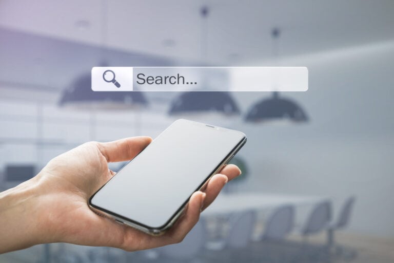 Hand holding a smartphone beneath a search bar, illustrating Google AI search